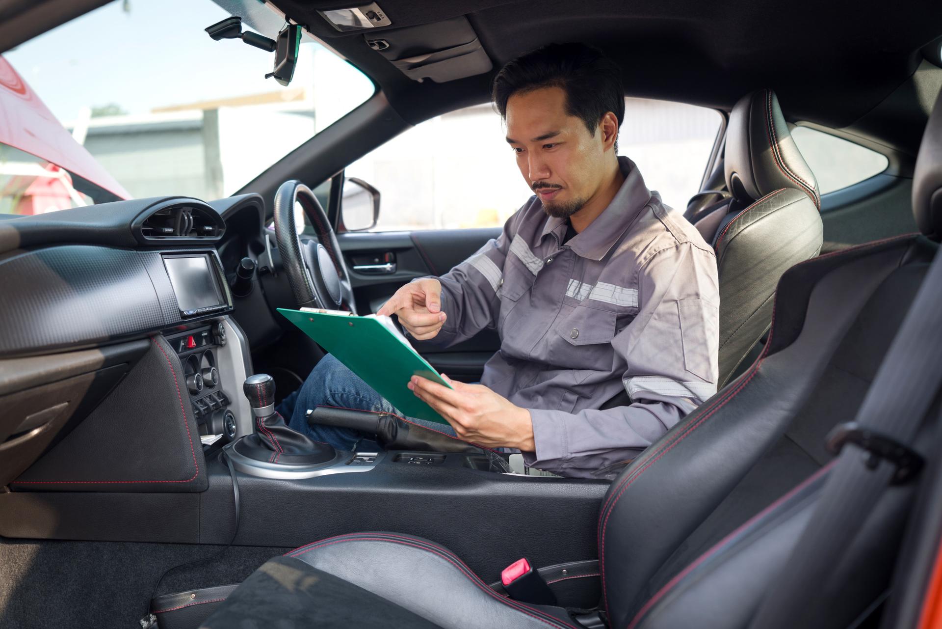 A mechanic in work uniform with a document clipboard, inspect a car coming for maintenance at a repair shop.